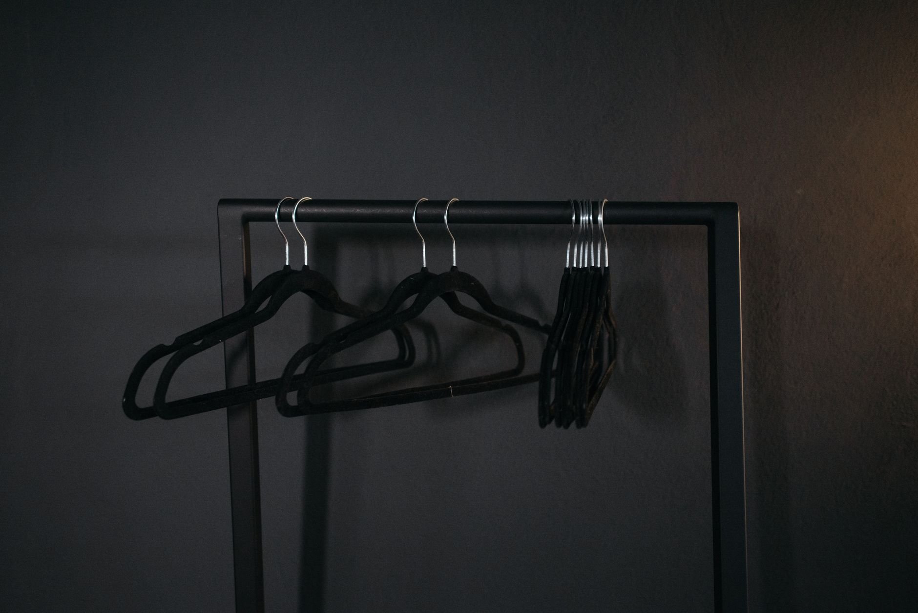 A minimalist design featuring black clothes hangers arranged on a metal rack against a dark backdrop.